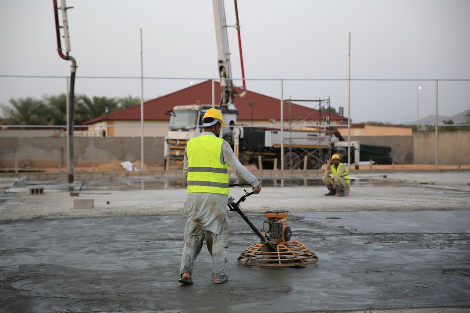 Workers smoothing concrete on a construction site with heavy machinery equipment.