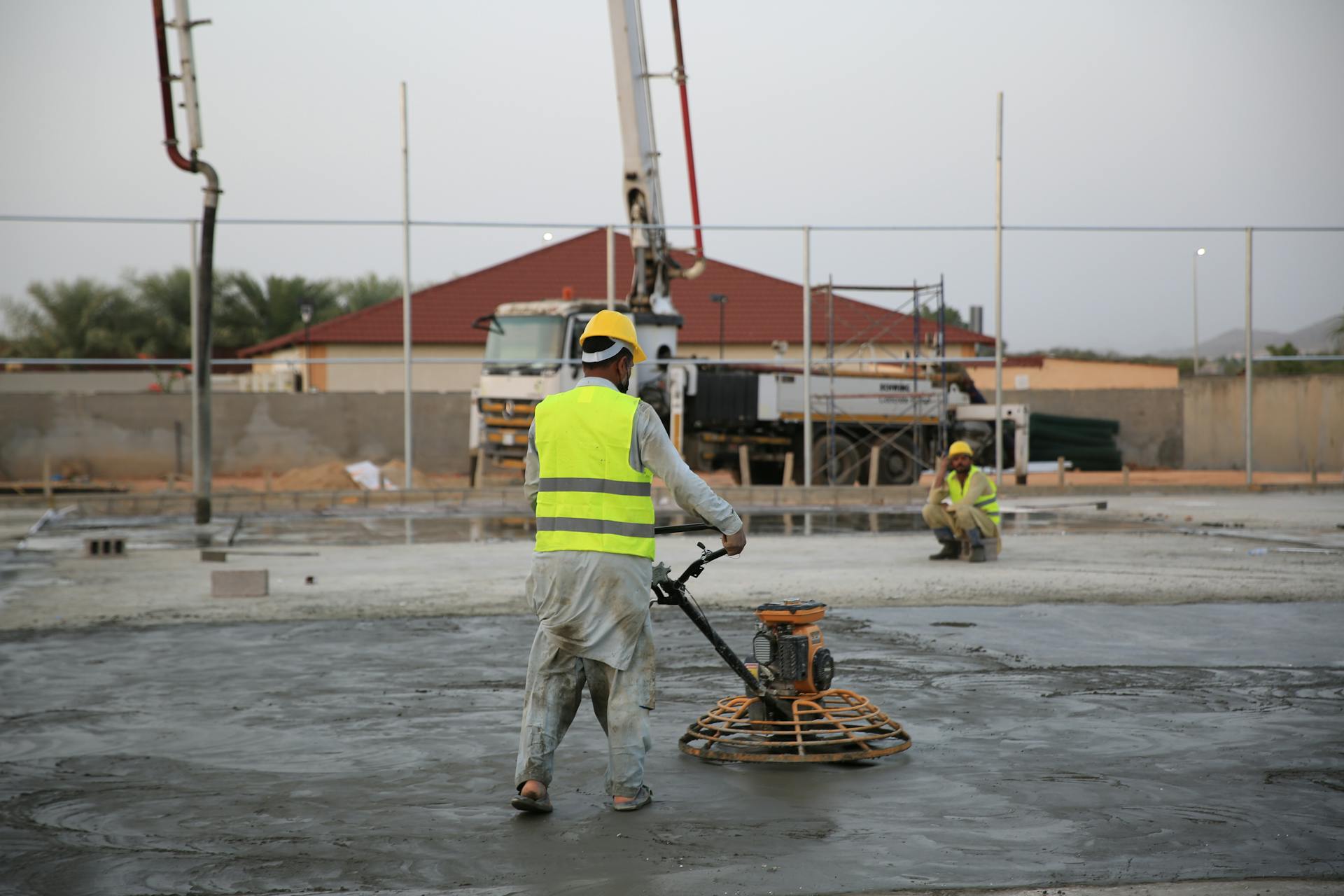Workers smoothing concrete on a construction site with heavy machinery equipment.