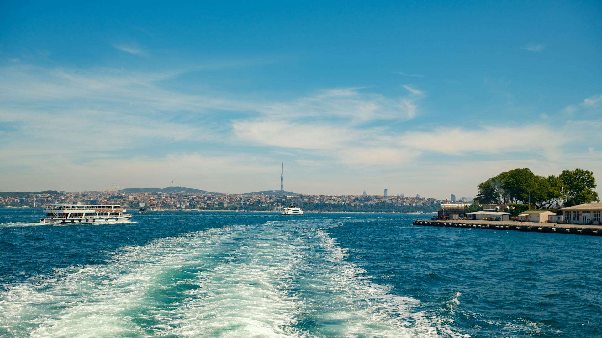 Boats travel across the serene Bosphorus Strait in Istanbul on a clear summer day, leaving trails on the water.