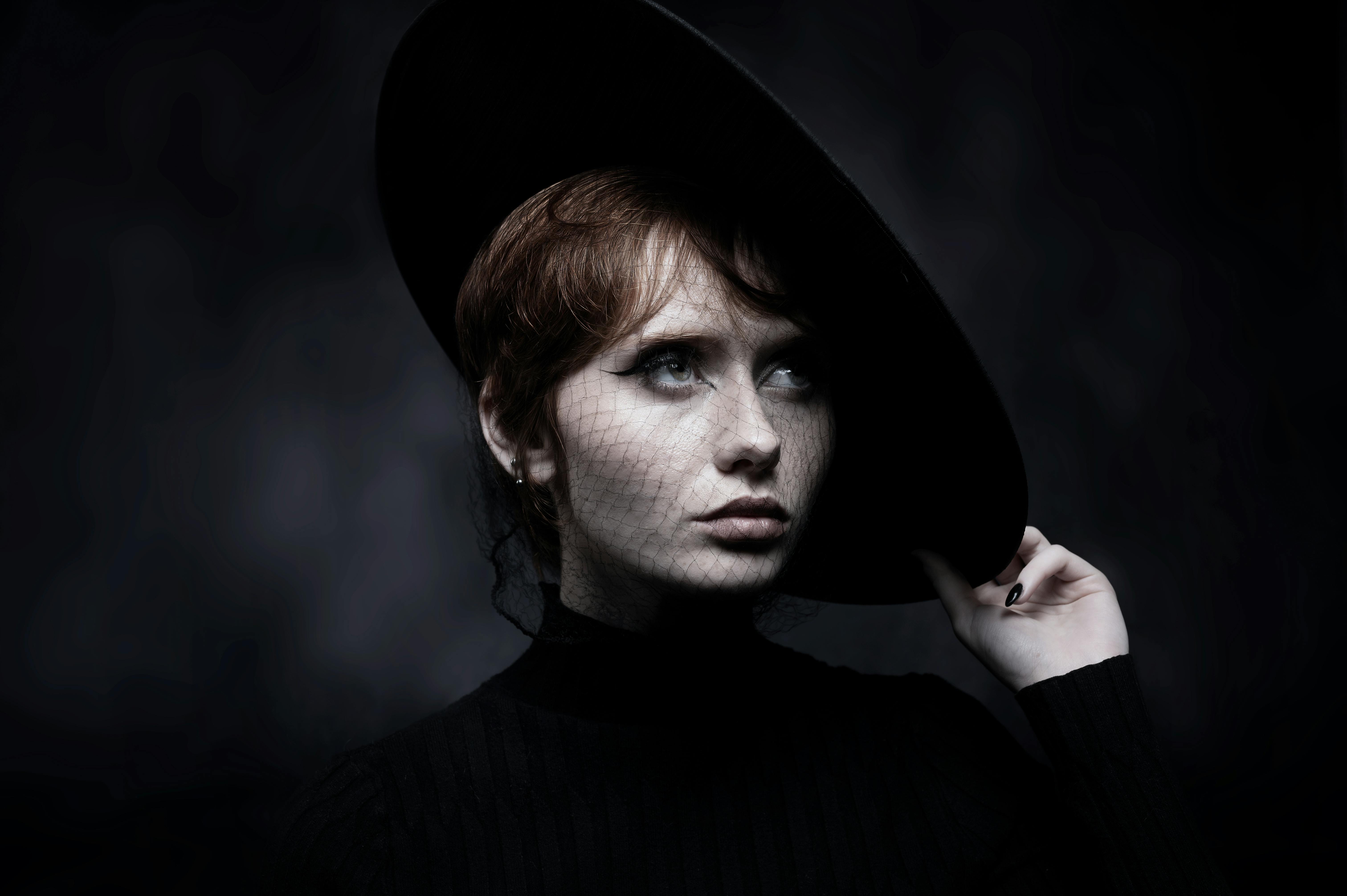 Moody portrait of a woman with a netted black hat and earrings.