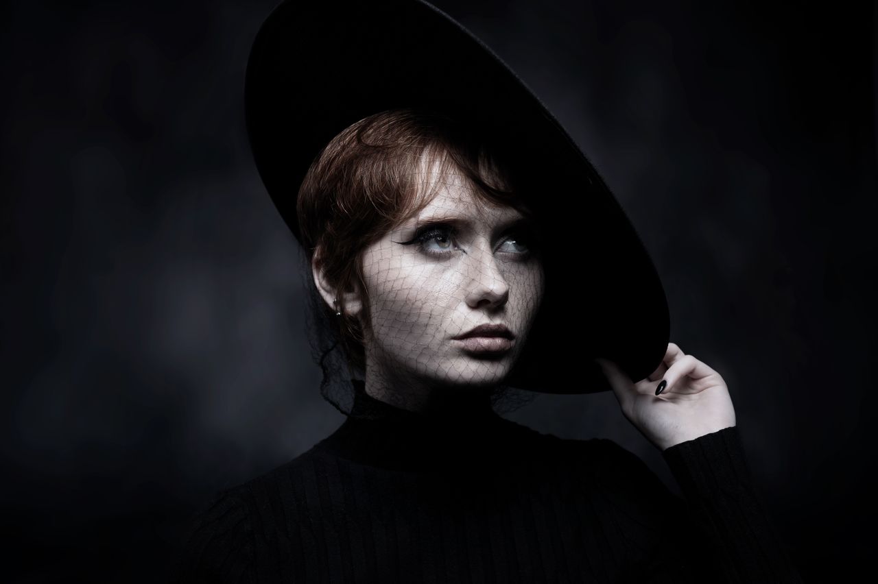 moody portrait of a woman with a netted black hat and earrings