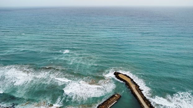 Stunning aerial shot of ocean waves crashing against a stone pier on a bright day.