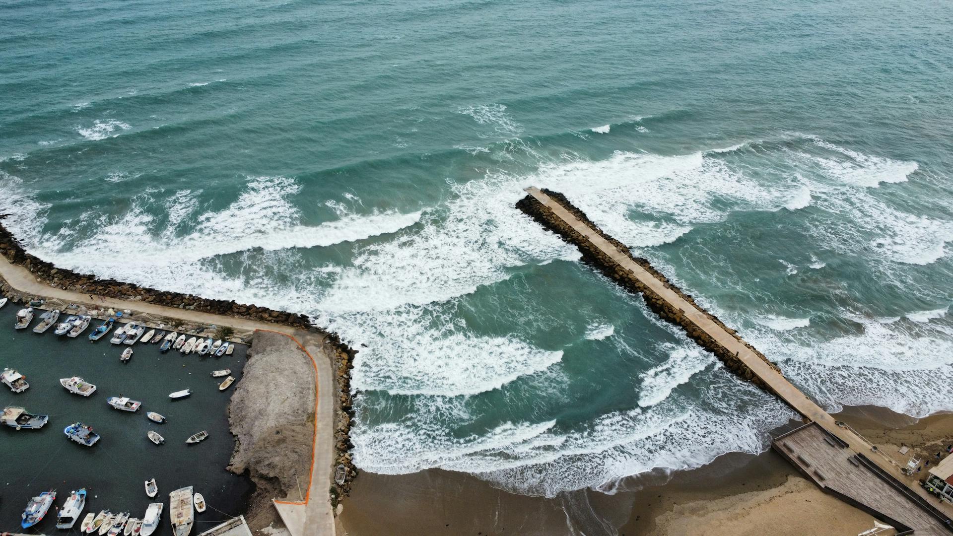 Stunning aerial shot of a coastal pier with waves and docked boats creating a scenic maritime view.