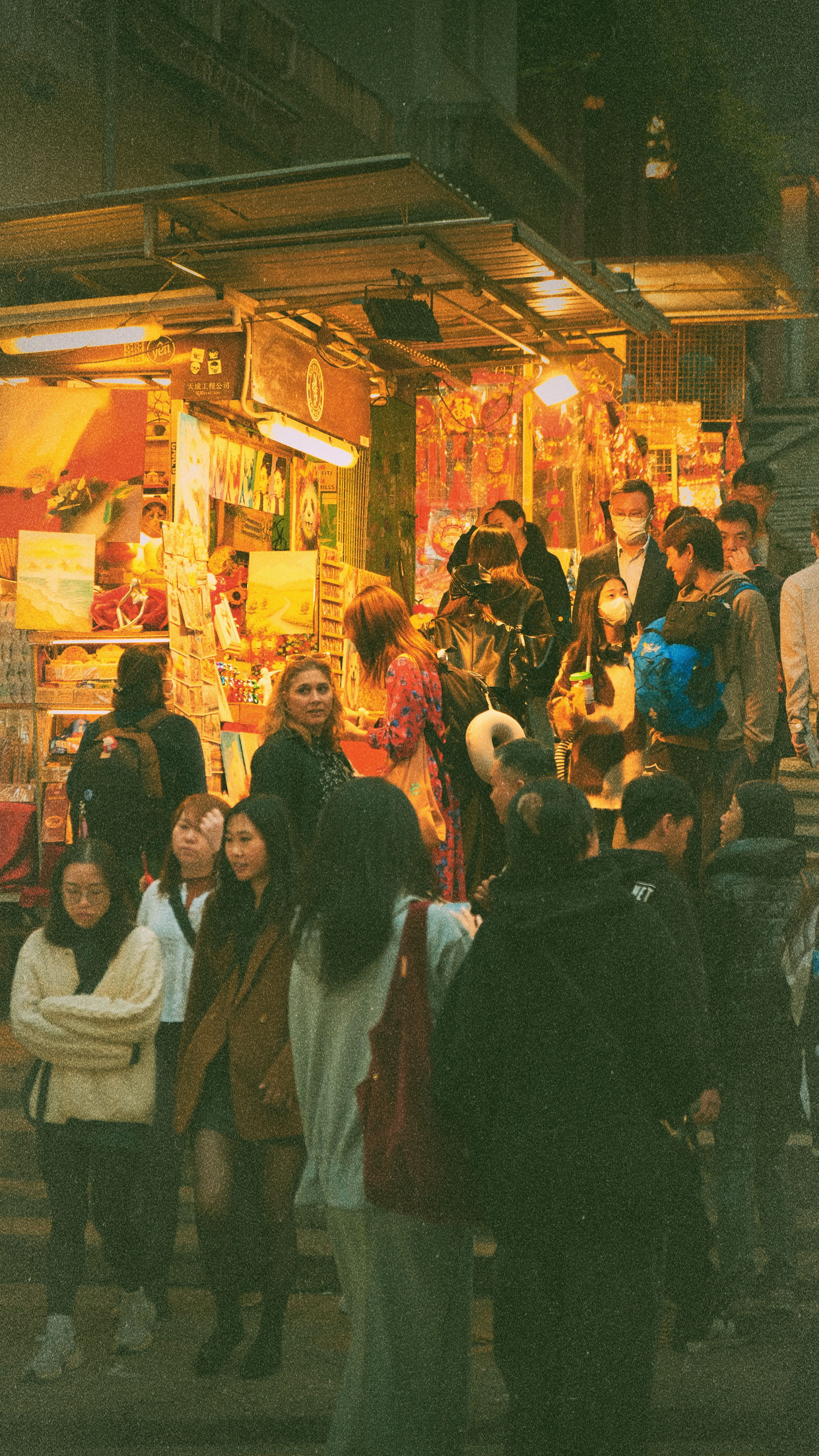 A bustling night market with crowded, brightly lit food stalls in an urban setting