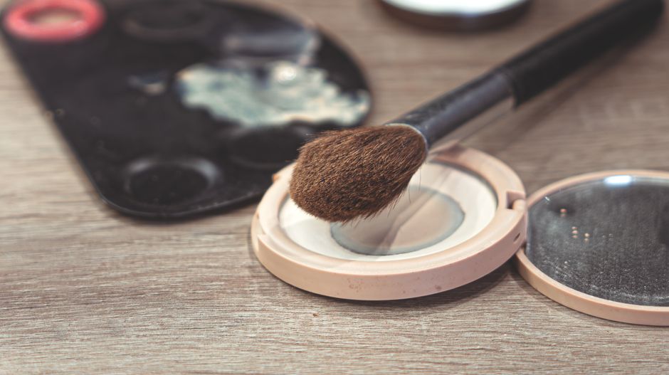 Close-up view of a makeup brush resting on an open compact powder on a wooden table.