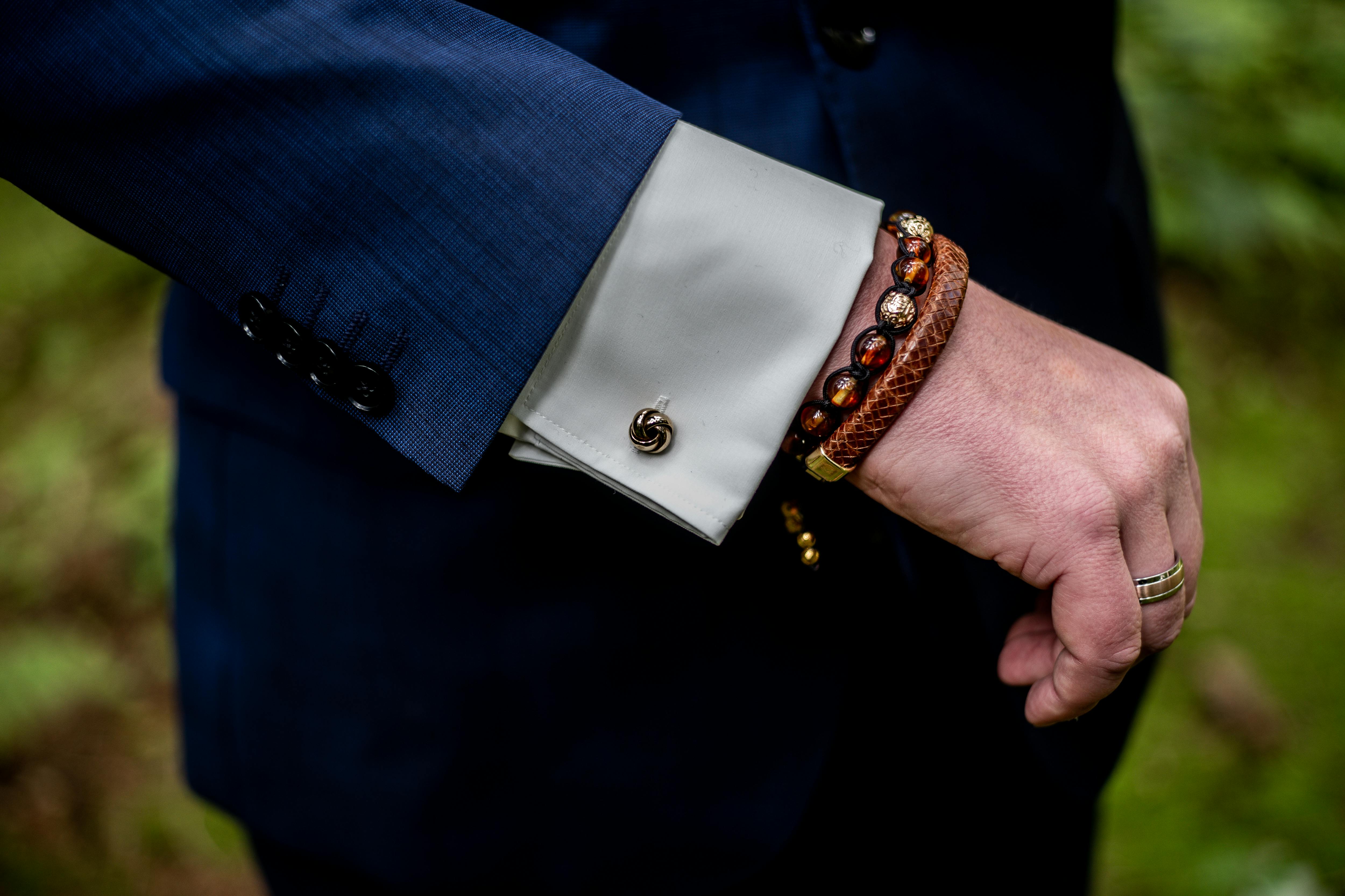A stylish close-up of a man's hand showing a suit sleeve, bracelet, and ring.