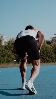 A male athlete gets ready at the starting line on a bright, sunny outdoor track.