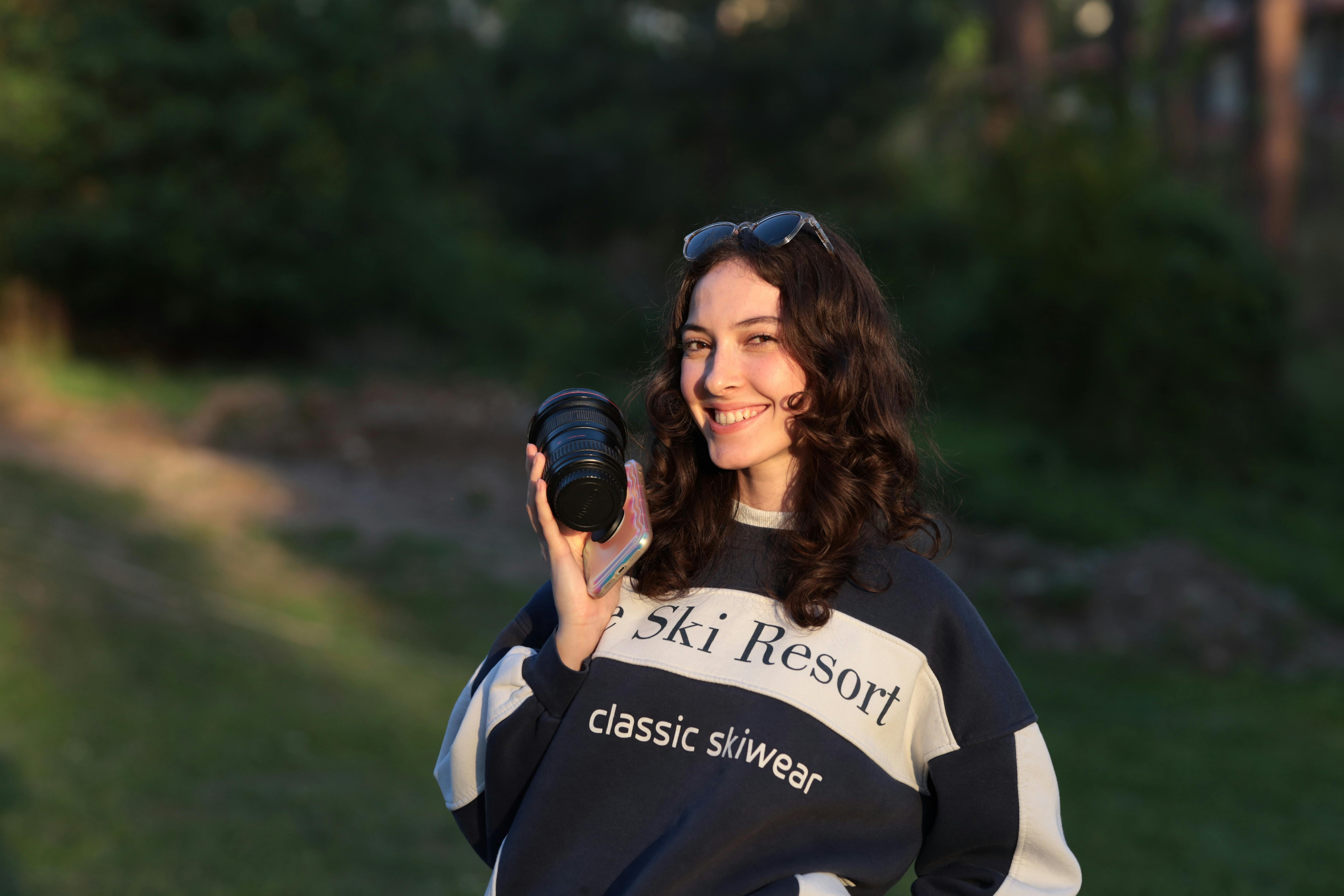 grátis Mulher sorridente segurando uma câmera em um ambiente natural ao ar livre durante o dia. Foto profissional