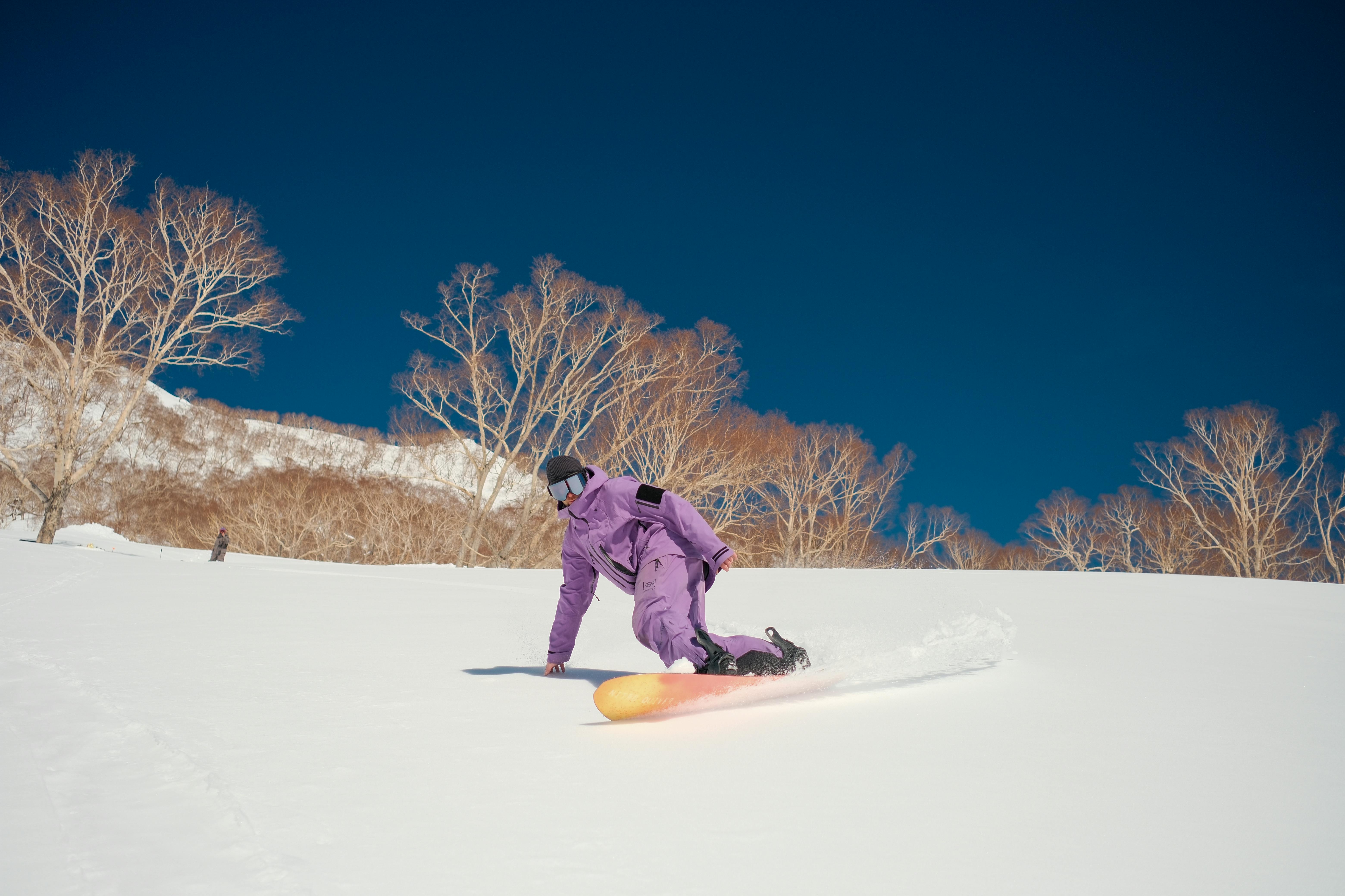 Snowboarder in vibrant attire carving through fresh snow in Hakuba, Japan.