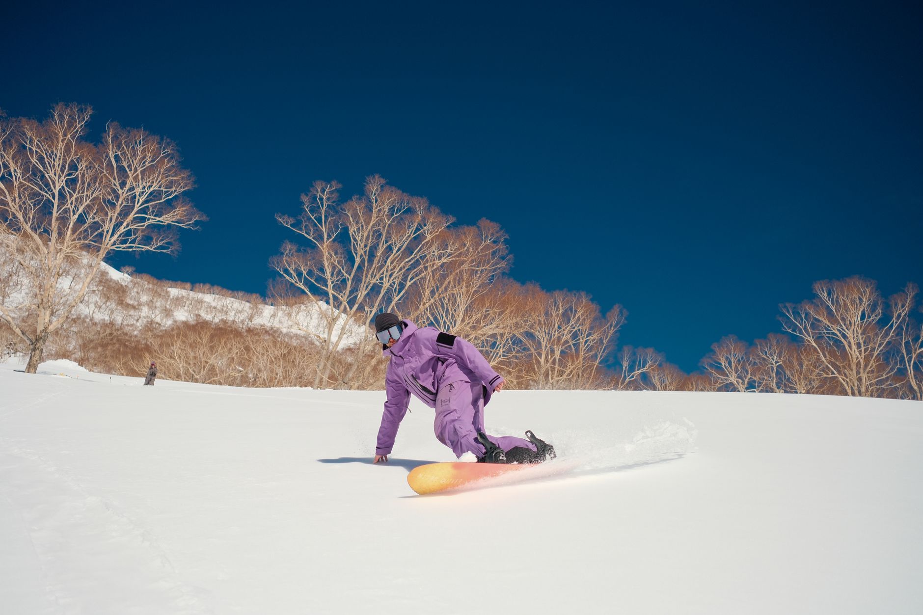 Snowboarder in vibrant attire carving through fresh snow in Hakuba, Japan.