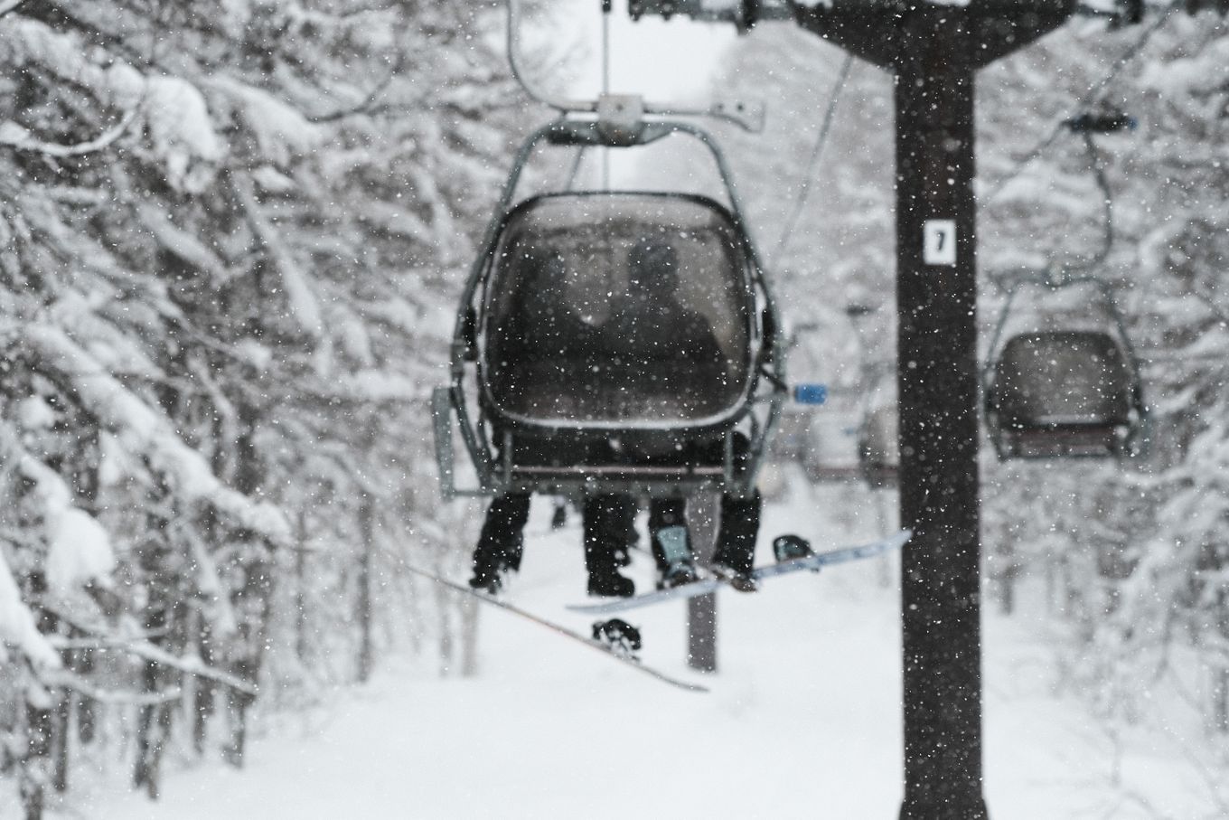 Skiers on a lift in a snowy forest in Japan, embracing the winter wonderland.