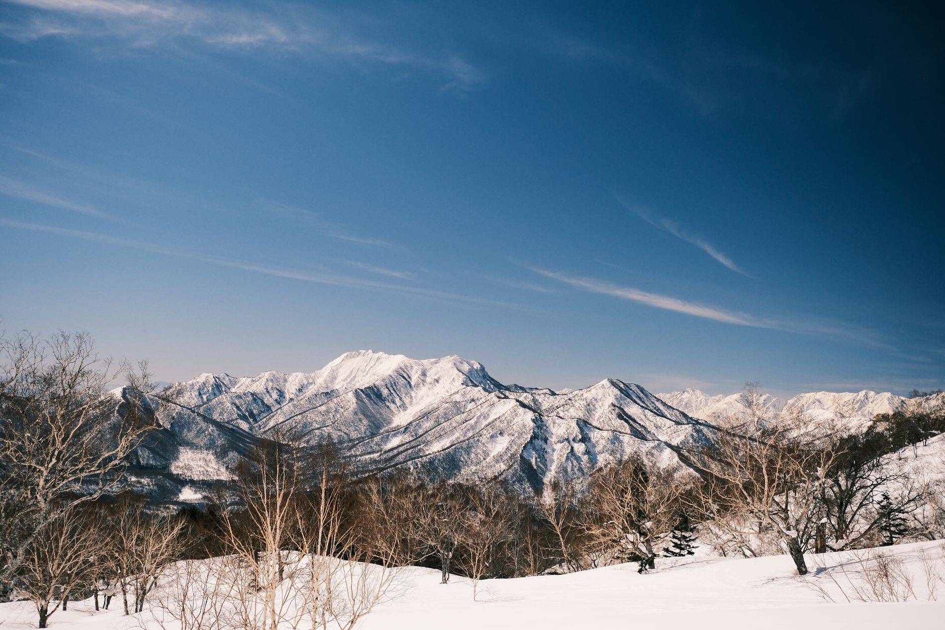 Scenic view of snow-covered Japanese Alps under a clear blue sky, perfect for winter sports.