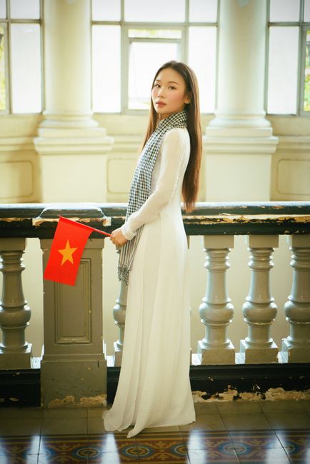 Mẹ Bầu Ăn Hạt Macca Được Không? Nên Ăn Bao Nhiêu Là Tốt Nhất? 3 A Vietnamese woman in traditional attire holds a flag inside Gia Long Palace, Ho Chi Minh City.
