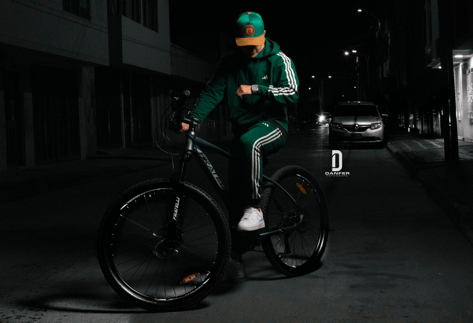 Man in vibrant green outfit rides bike at night in Bogotá's urban setting.