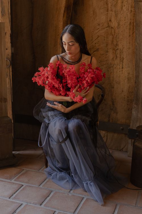 Free A woman sitting indoors, holding vivid red flowers, captured in soft natural light, exuding a calm and tranquil mood. Stock Photo