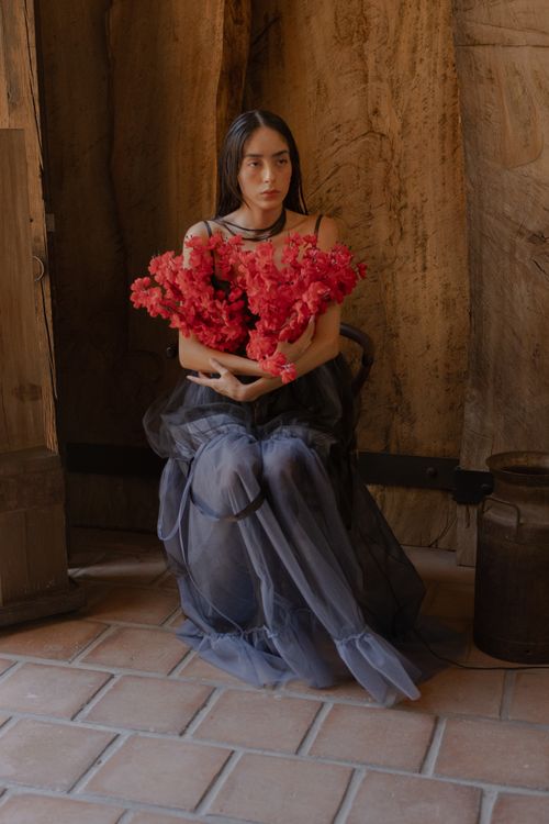 Free A young woman in elegant dress holding red flowers in an indoor rustic setting. Stock Photo
