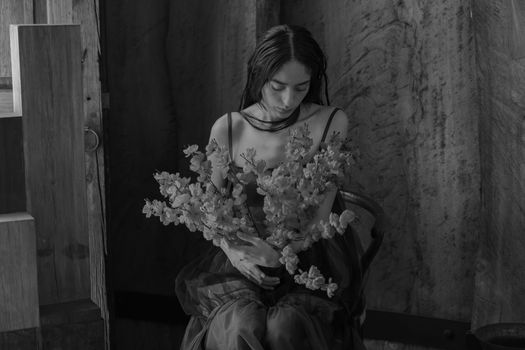 A woman holding a bouquet of flowers in a contemplative black and white setting.