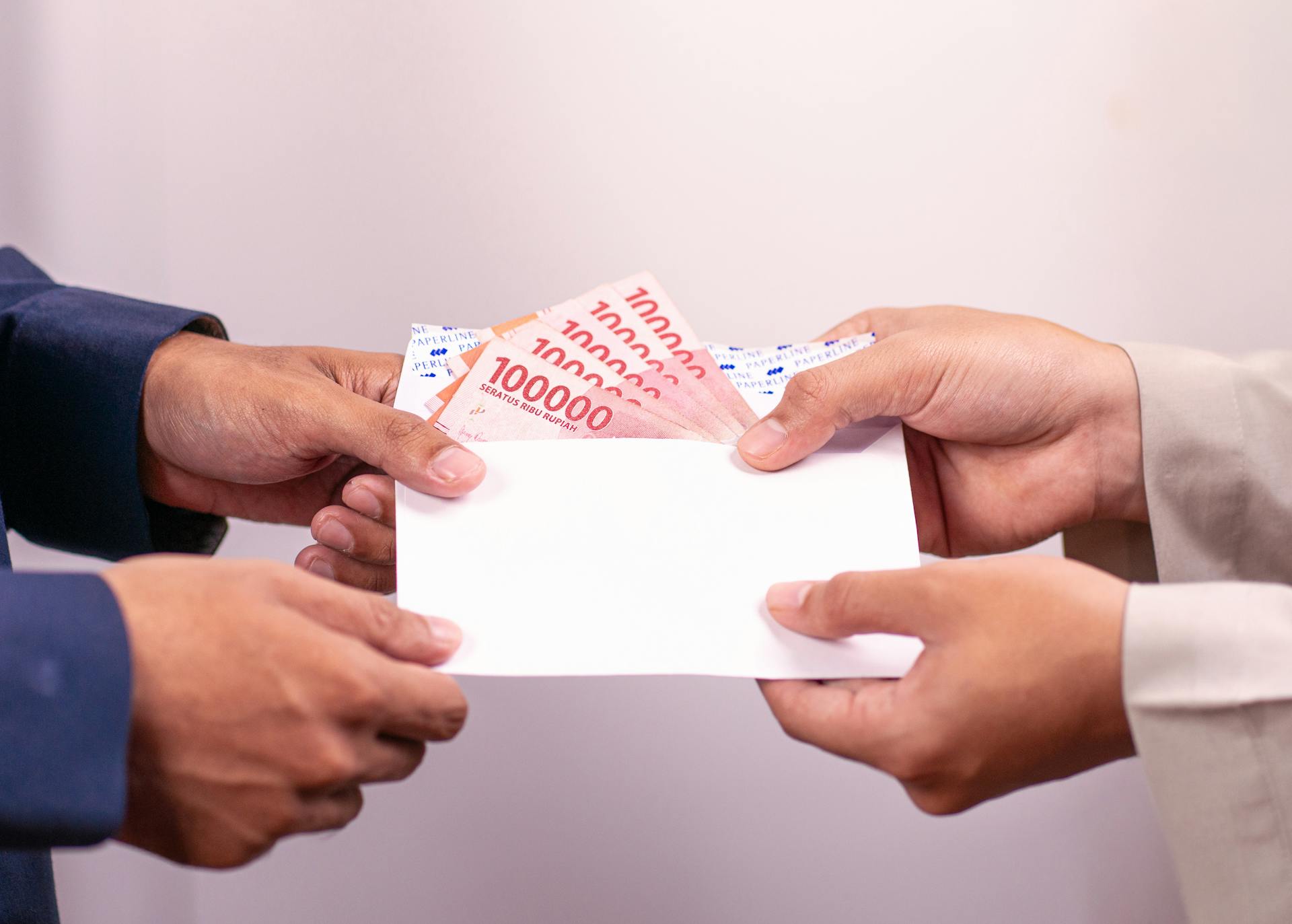 Hands exchanging an envelope with Indonesian Rupiah, highlighting financial transactions.
