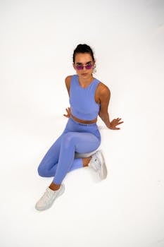 Fashion portrait of a woman in purple sportswear and sunglasses on a white background.