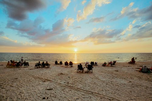 Free A serene view of people relaxing on a sandy beach at sunset, enjoying the tranquil ocean scenery. Stock Photo