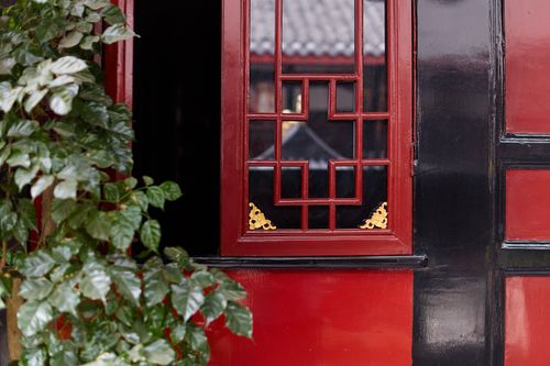 Free Close-up of a traditional red and black Asian window with foliage, showcasing intricate wooden design and cultural elements. Stock Photo