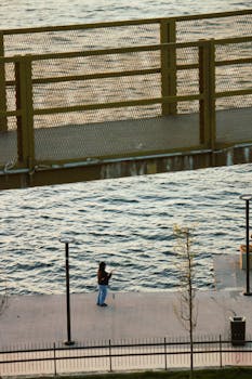 Person fishing alone on a waterside pathway during sunset creates a tranquil scene.