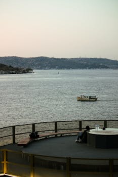 Couple enjoys serene sunset view over Istanbul's Bosphorus with distant hills and boat.