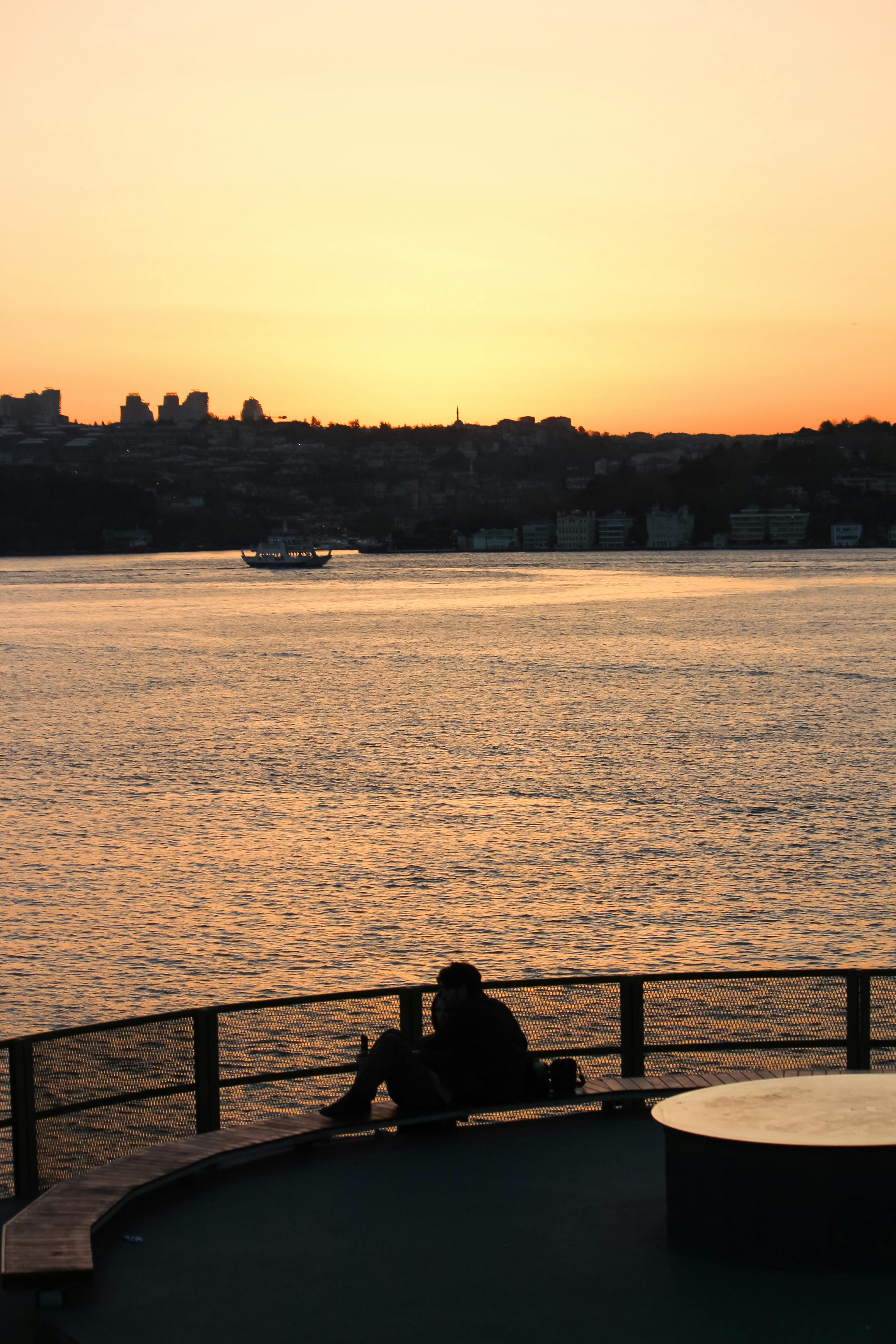 Silhouette of a person sitting by the water at sunset in Istanbul, showcasing vibrant orange hues.