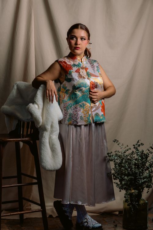 Free Portrait of a stylish woman in a vibrant floral vest, leaning on a chair indoors. Stock Photo