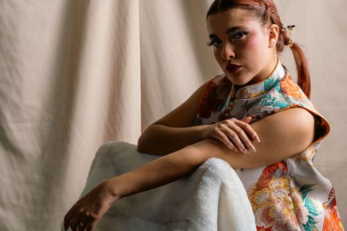 Free Portrait of a young woman in colorful floral attire sitting indoors, exuding elegance and style. Stock Photo