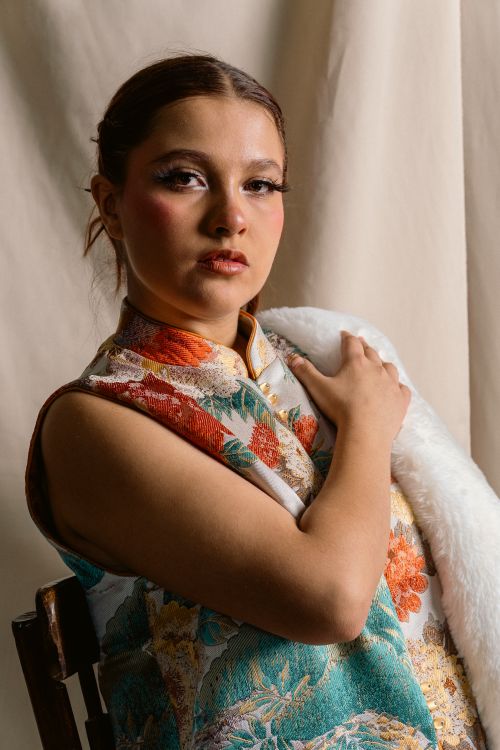 Free A young woman in a colorful floral dress posing elegantly against a neutral background. Stock Photo