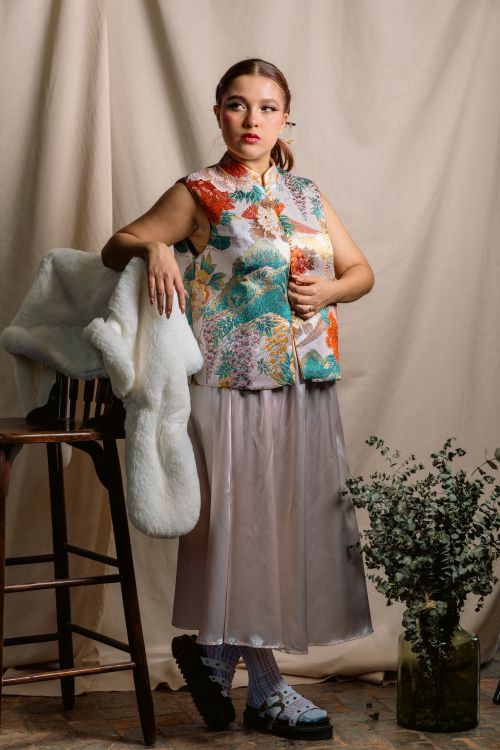 Free Portrait of a woman indoors in colorful floral attire leaning on a chair, embodying elegance. Stock Photo