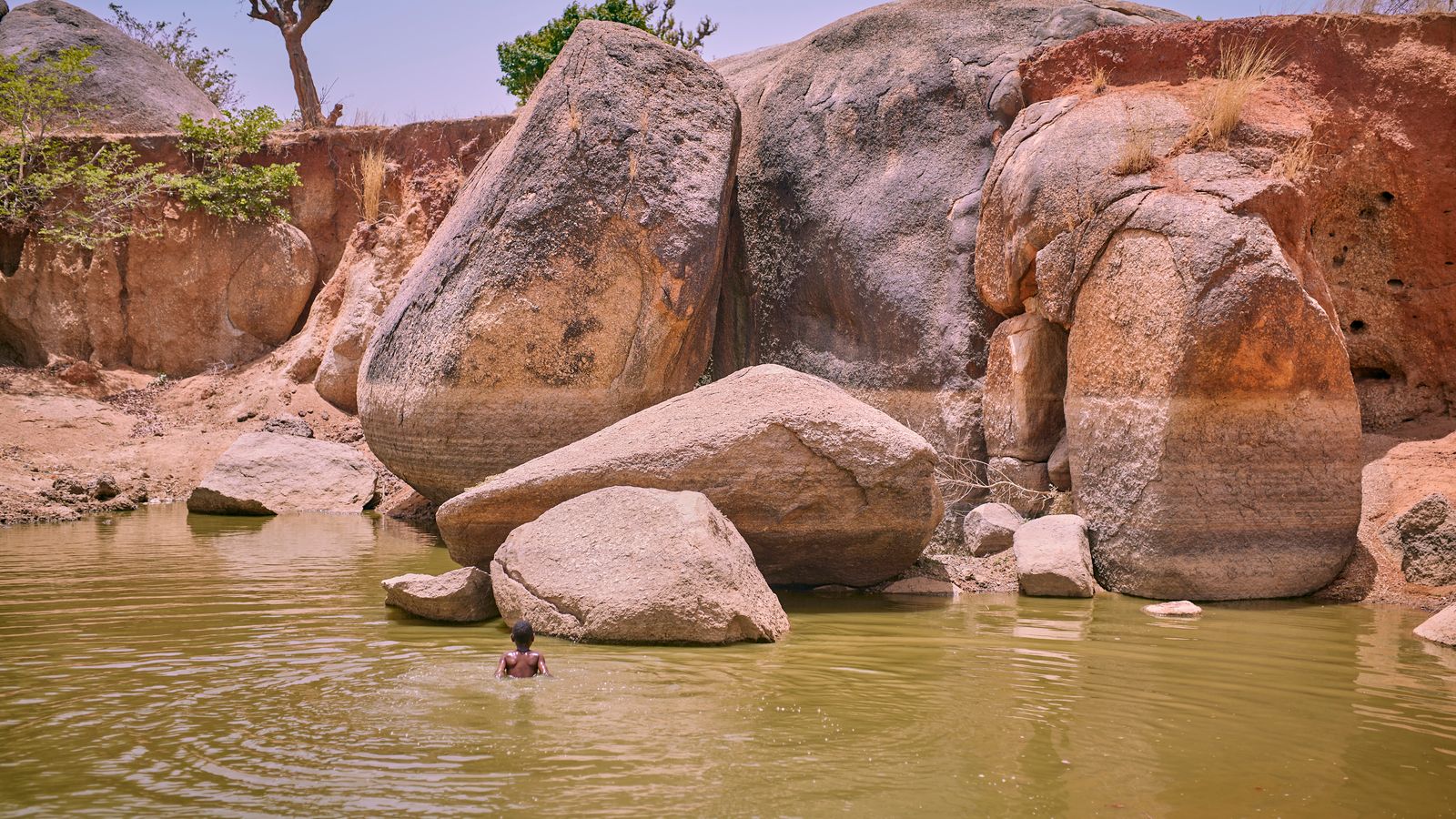 Man swimming in rocky desert oasis pool, Guinea