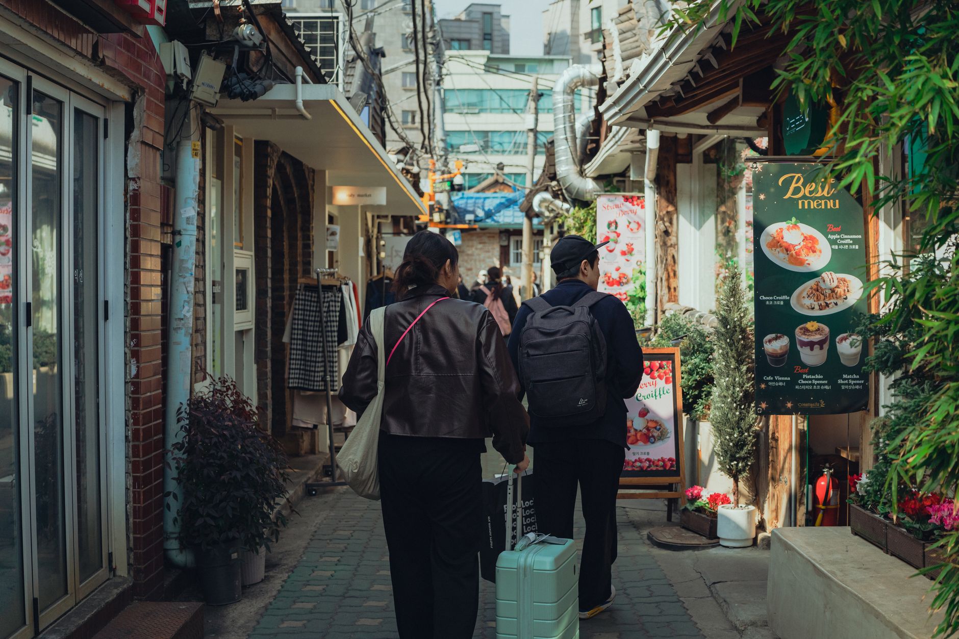 Two people walking through a vibrant alleyway in Seoul, showcasing food and local shops.