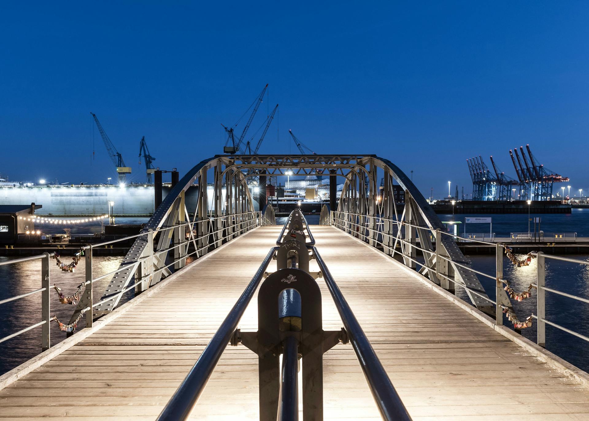 Captivating nighttime view of a bridge in Hamburg's harbor, showcasing industrial cranes and waterfront lights.