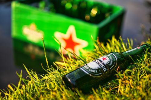 Free A Heineken beer bottle reclines on grass by the lake, ideal for summer leisure. Stock Photo