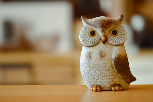 Close-up of a ceramic owl figurine placed on a wooden table indoors.