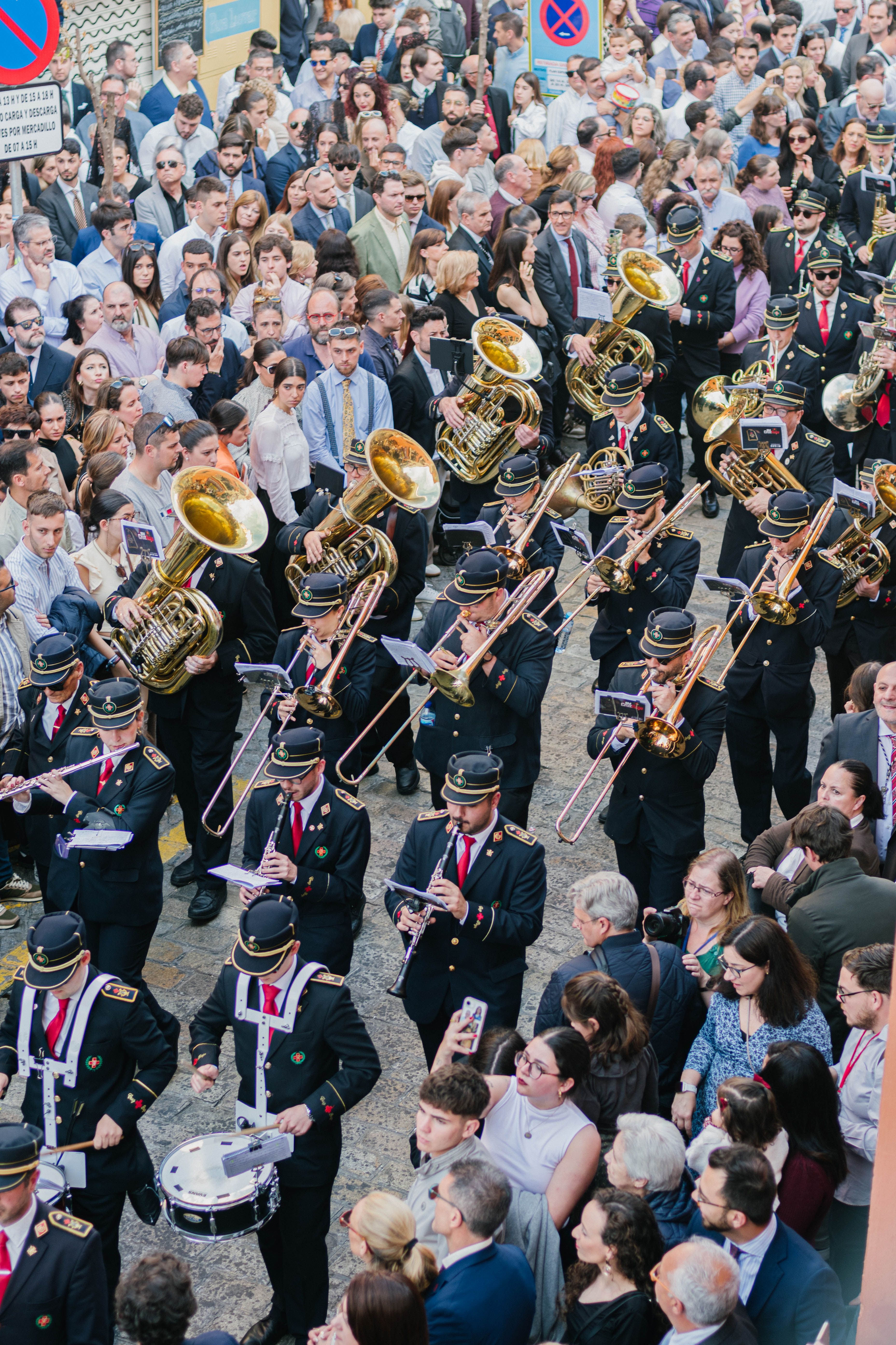 A vibrant brass band leads a parade through the crowded streets of Seville, Spain.