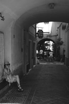 Black and white photo of a serene Italian alleyway with archway and people.