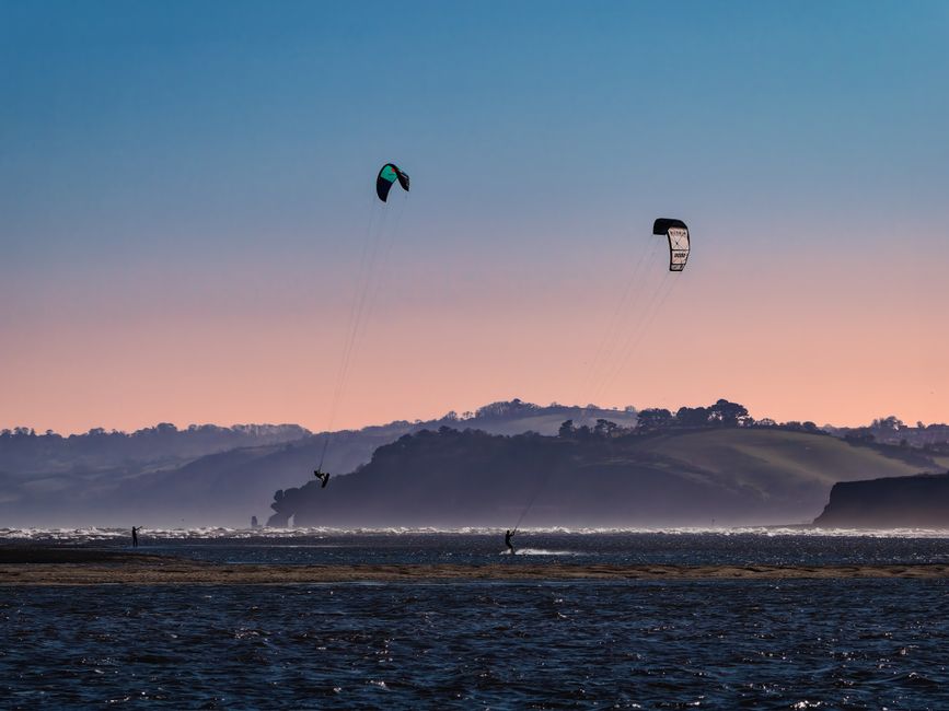 Vibrant kitesurfing scene at sunset on Exmouth beach, capturing dynamic water sports in beautiful coastal landscape.