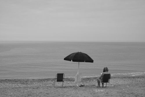 Free Serene black and white beach scene with a lone woman under an umbrella in Italy. Stock Photo