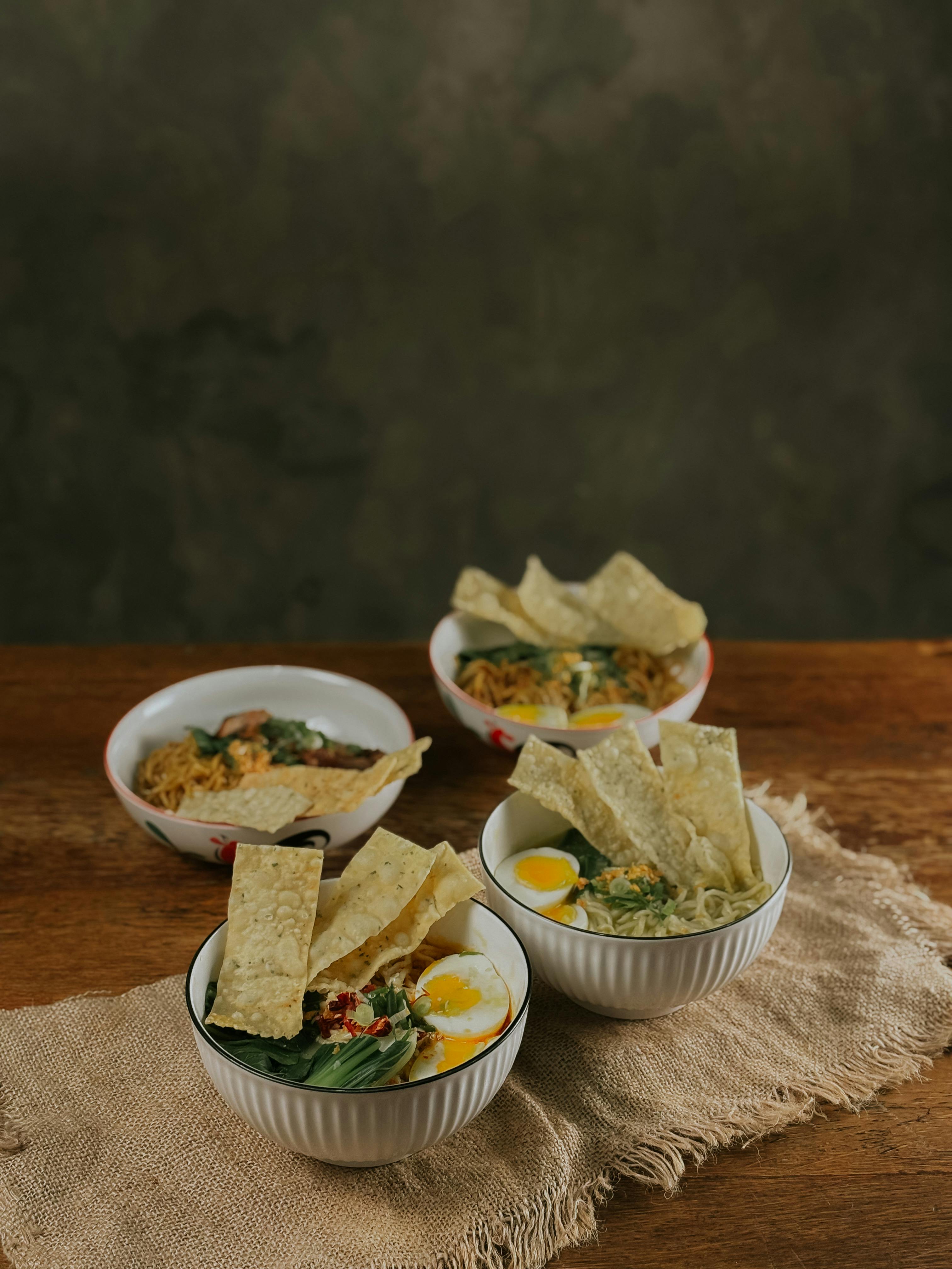 Delicious Asian noodle soup bowls with boiled eggs and crispy crackers on a rustic table