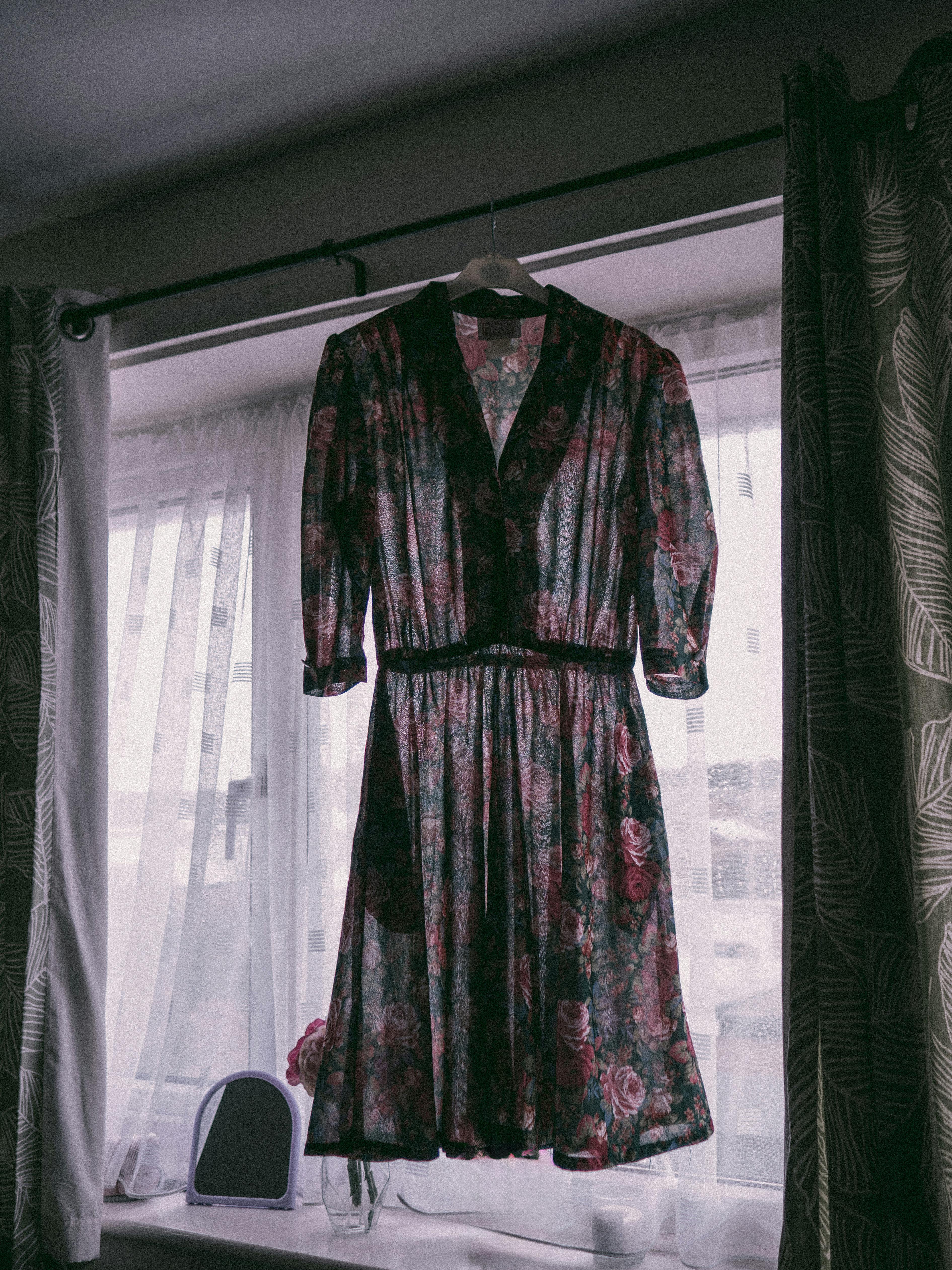 A vintage floral dress hangs beautifully by a window, casting soft shadows.
