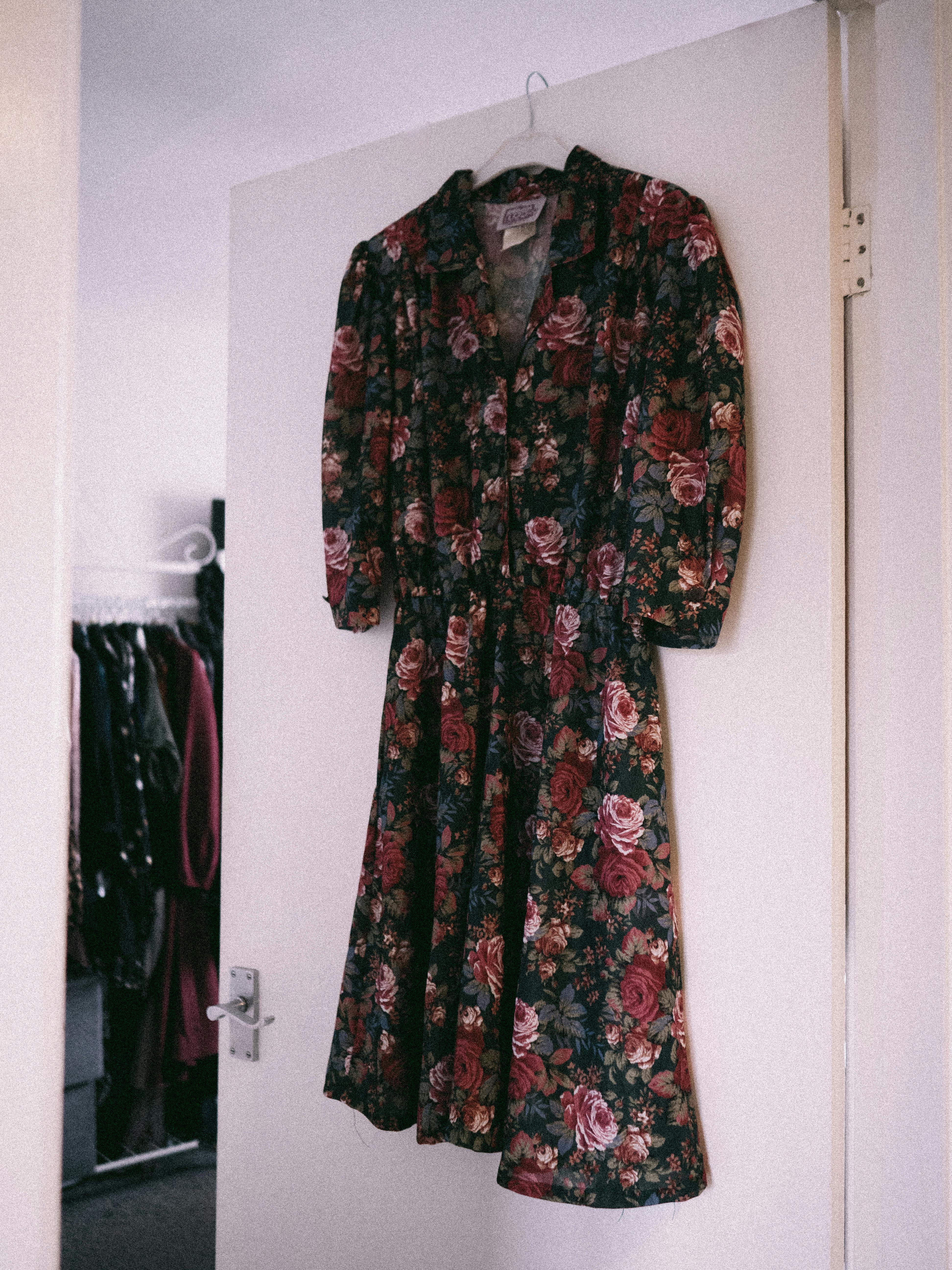 A classic vintage floral dress hangs elegantly in a softly lit closet setting.
