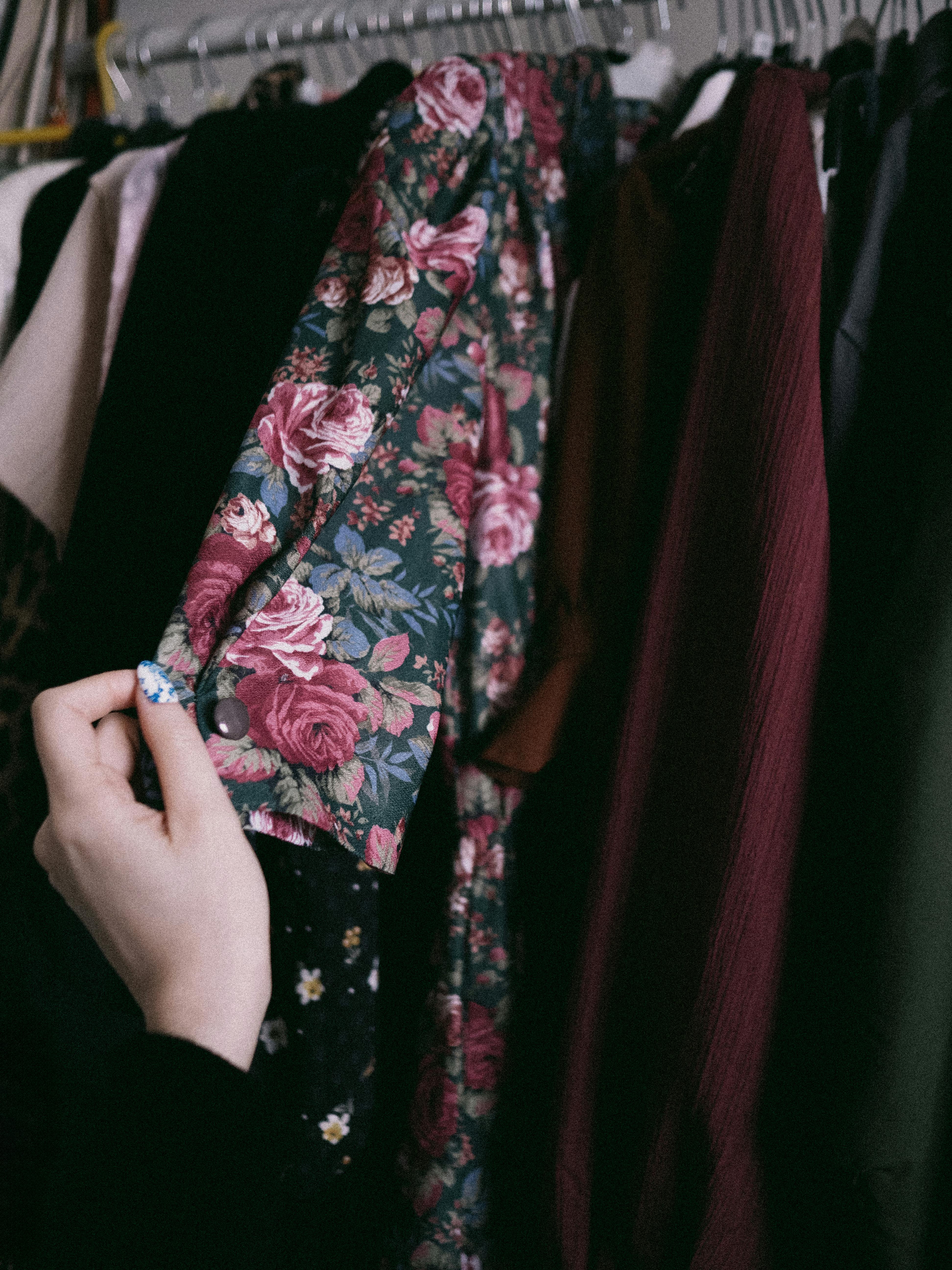 A hand pulling a floral vintage dress from a crowded rail, like the moment taste becomes selection