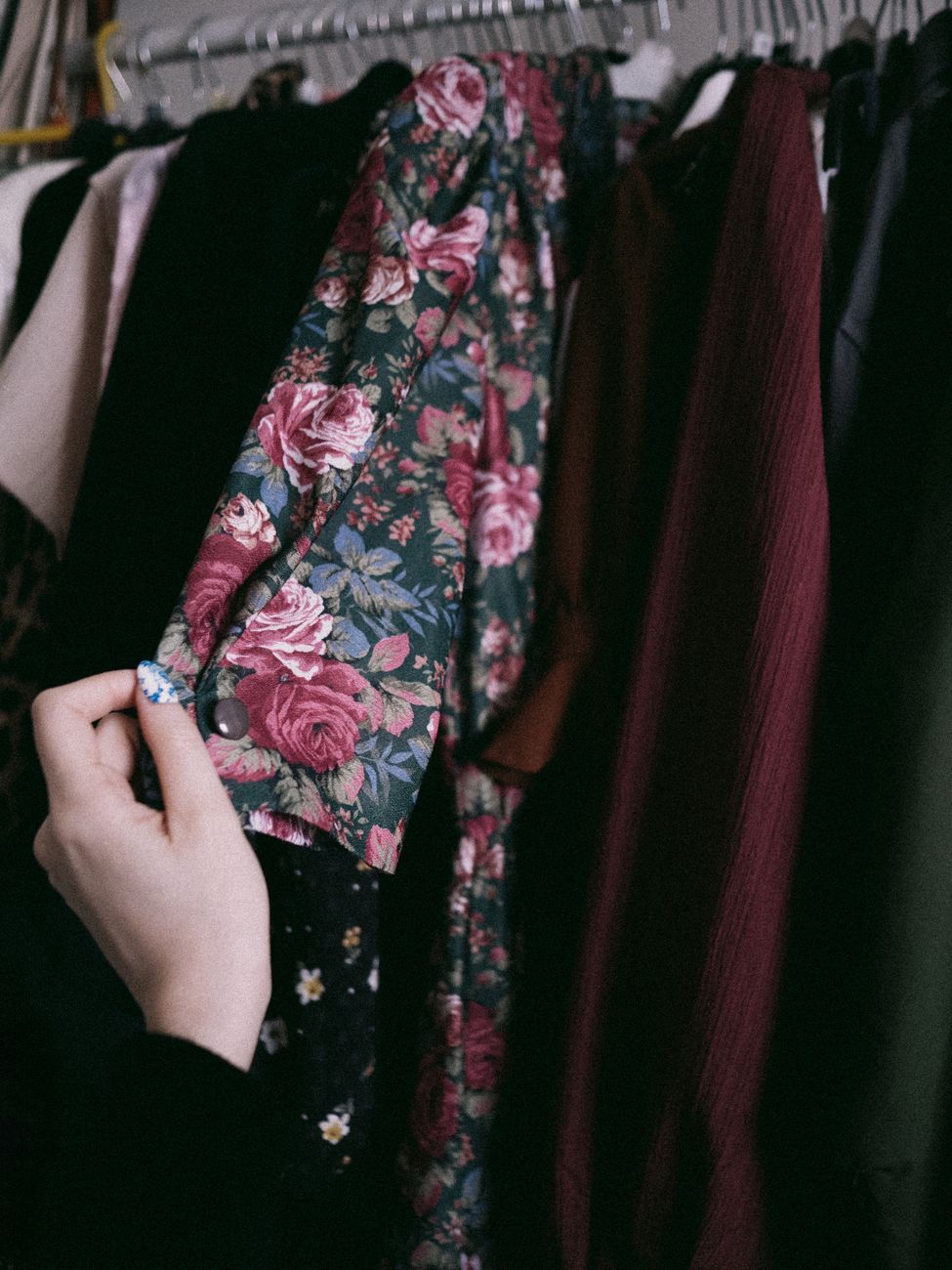 A hand pulling a floral vintage dress from a crowded rail, like the moment taste becomes selection