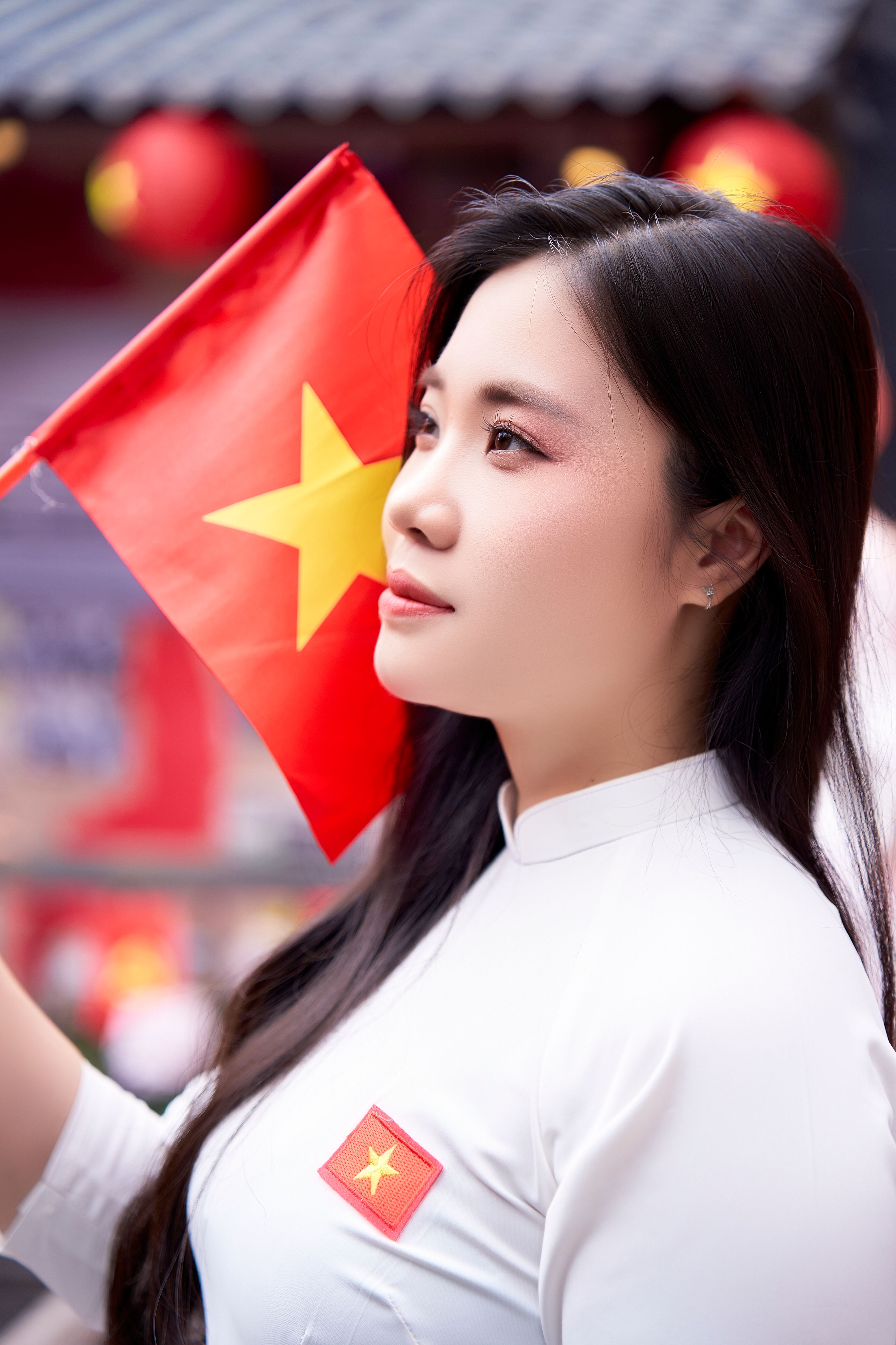 Portrait of a young woman in traditional attire holding a Vietnamese flag, symbolizing national pride.