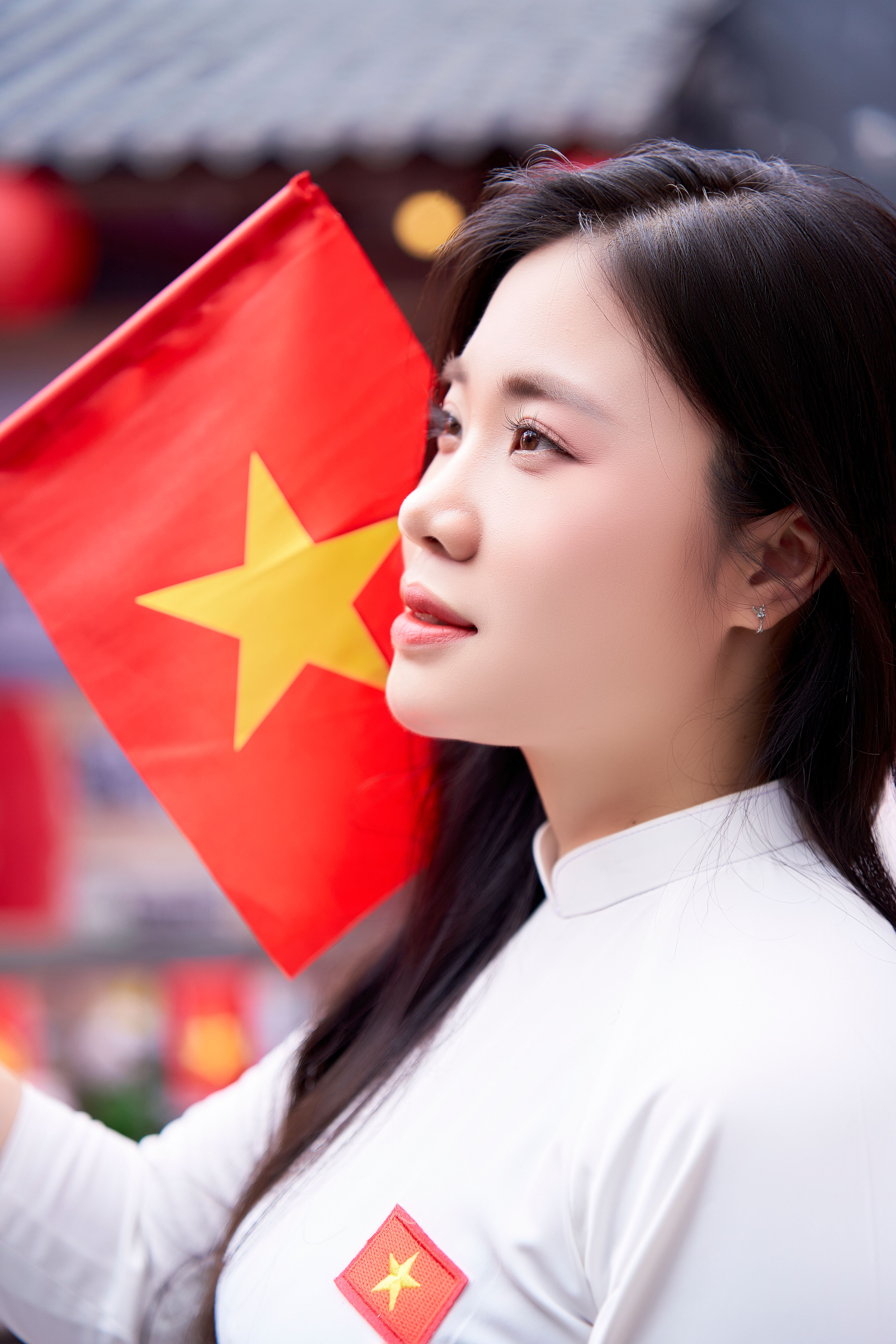 A young woman in traditional attire holding a Vietnamese flag in a vibrant outdoor setting.
