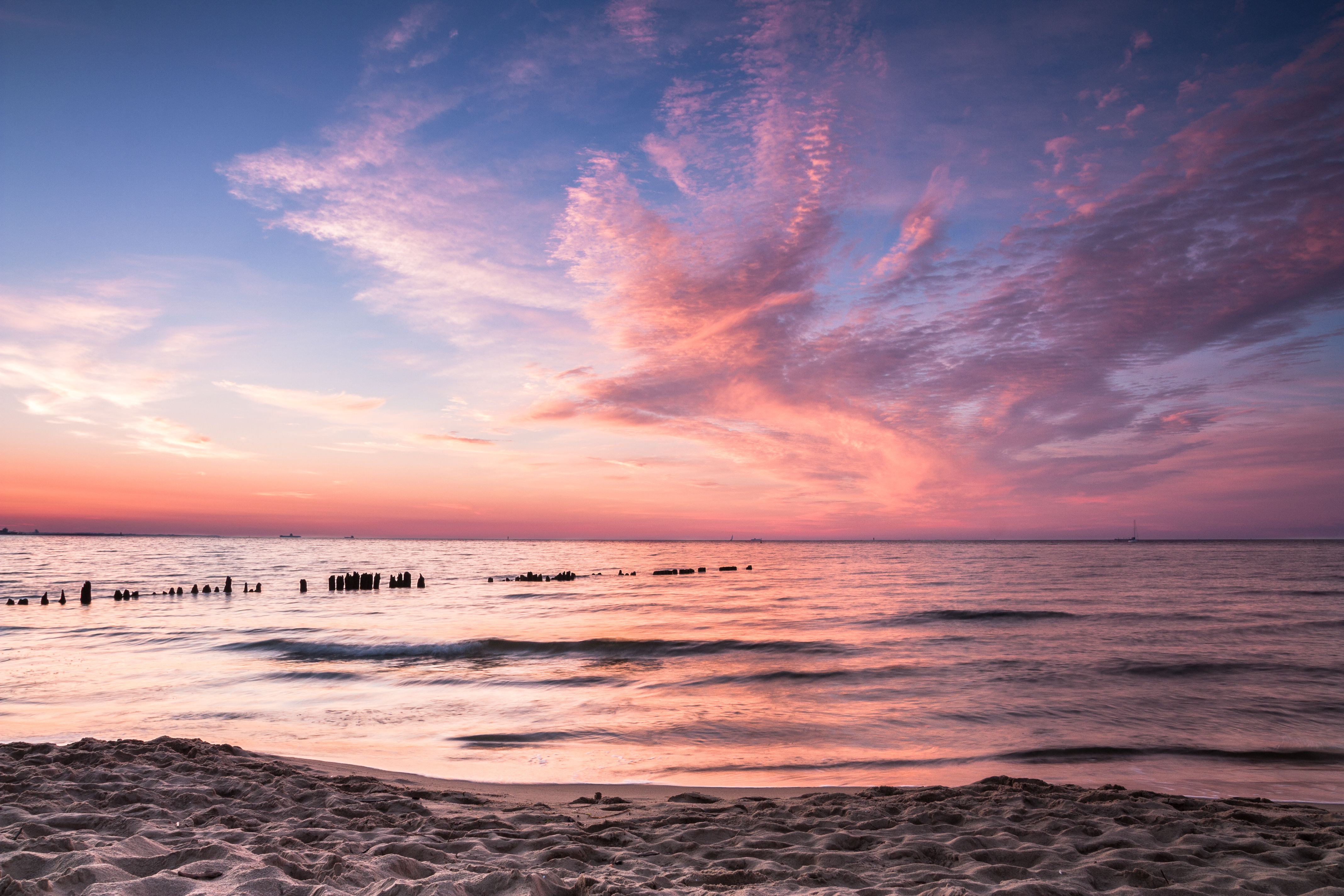 Capture the serene beauty of a Gdańsk beach at sunset with vibrant pink and orange skies.