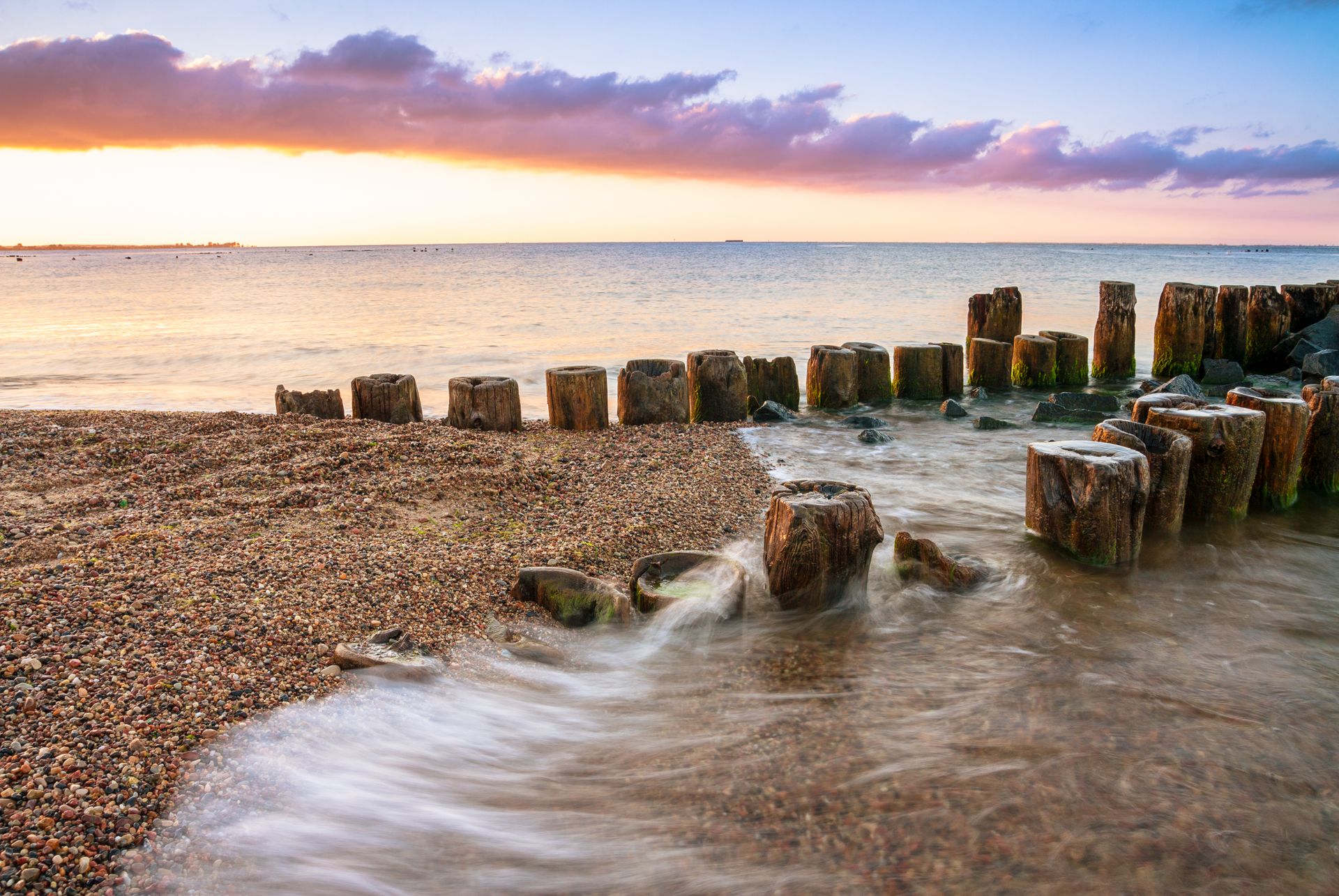 Sunset view of the Baltic Sea with wooden breakwaters and pebbles in Gdańsk, Poland.